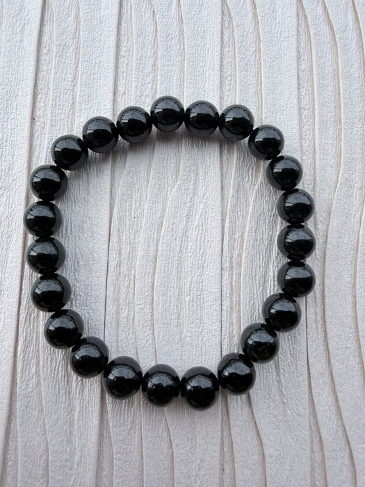 Dreamy Jade polished black obsidian beaded elastic bracelet on a textured light background