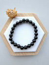 Dreamy Jade black obsidian beaded bracelet with polished round stones on a white hexagonal display with a dried flower.
