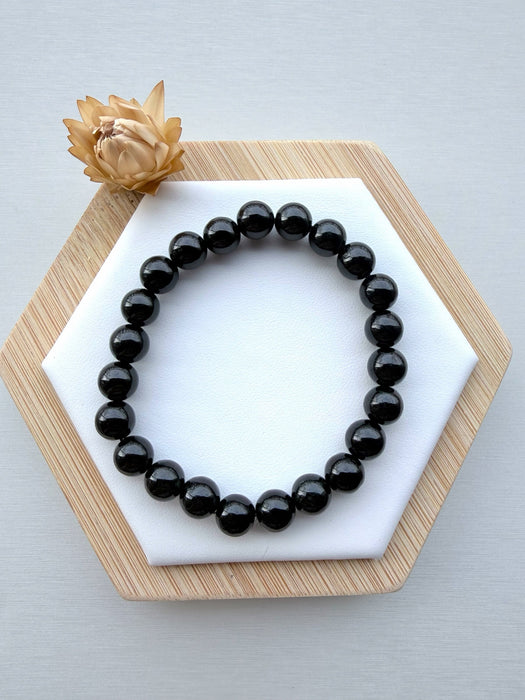 Dreamy Jade black obsidian beaded bracelet with polished round stones on a white hexagonal display with a dried flower.