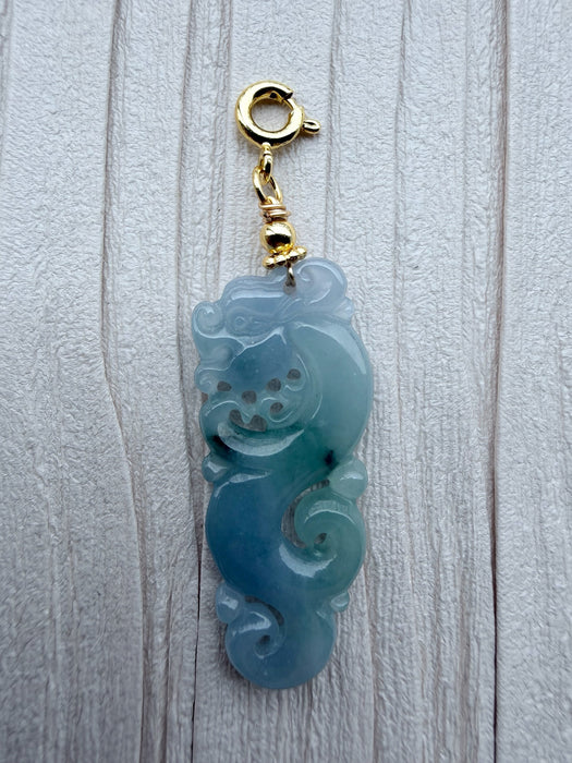 Dreamy Jade blue-green jadeite dragon pendant with a gold-tone clasp on a textured white background