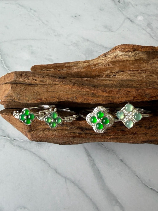 Dreamy Jade clover-inspired rings featuring vibrant green jade stones set in polished silver on a rustic wood base.