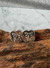 Dreamy Jade clover stud earrings with silver-tone beaded edges and textured backs resting on a piece of natural wood.