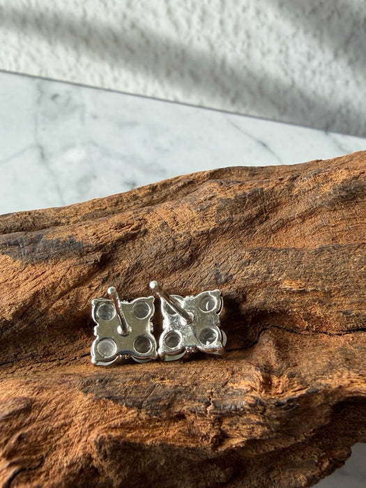 Back view of Dreamy Jade clover stud earrings featuring silver-tone metal posts resting on a textured wooden surface.