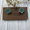 Dreamy Jade clover stud earrings featuring soft green stone inlay and a delicate beaded metal edge on a wooden stand.