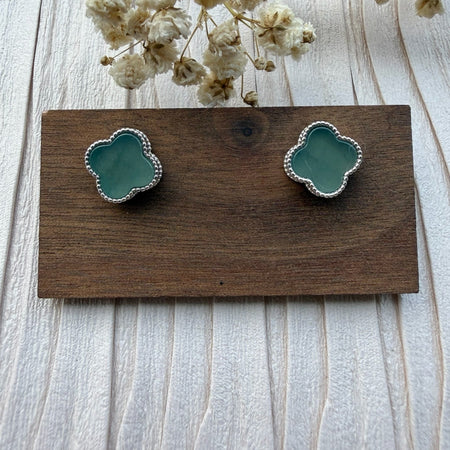 Dreamy Jade clover stud earrings featuring soft green stone inlay and a delicate beaded metal edge on a wooden stand.