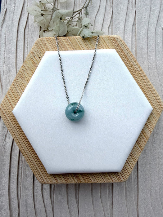 Dreamy Jade donut pendant necklace featuring a translucent green jade stone on a silver-tone chain on a display stand.