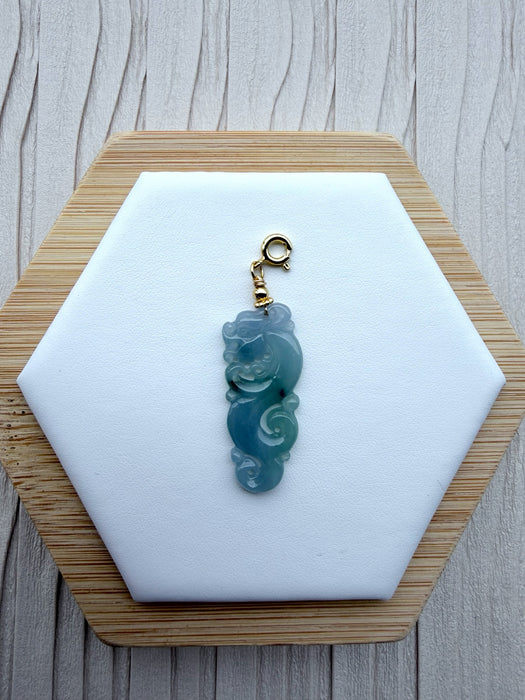 Dreamy Jade mythical dragon pendant carved from translucent blue-green jadeite with a gold-tone clasp on a display.
