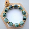 Dreamy Jade beaded bracelet with polished green natural jade stones and gold-tone spacers on a wooden display stand.