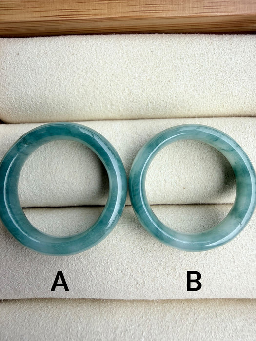 Dreamy Jade pair of polished natural green jadeite stone bangles with unique marbling on a beige jewellery tray