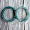 Dreamy Jade pair of polished natural green jadeite stone bangles with unique marbling on a textured white background