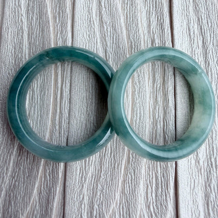 Dreamy Jade pair of polished natural green jadeite stone bangles with unique marbling on a textured white background
