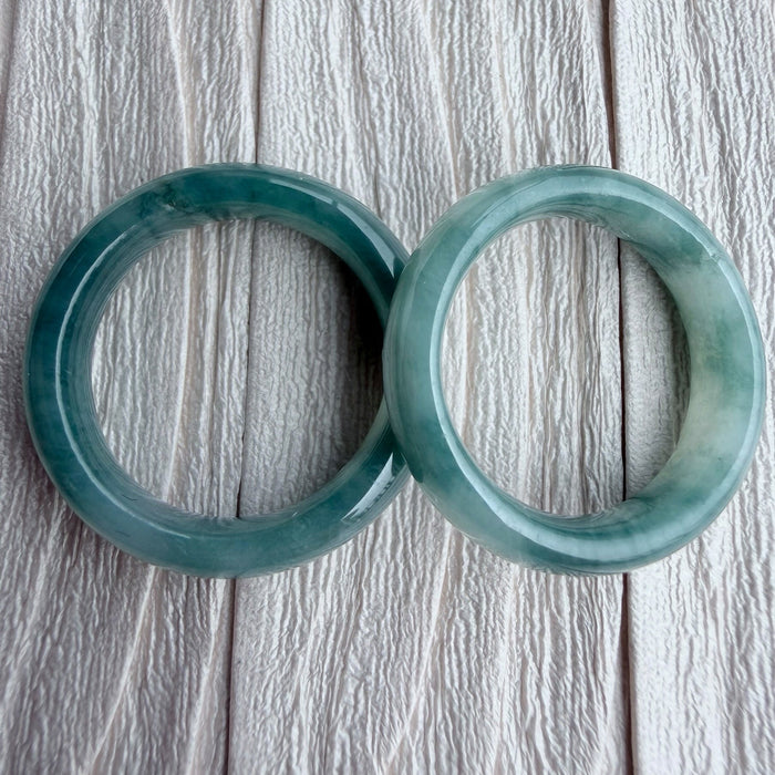 Dreamy Jade pair of polished natural green jadeite stone bangles with unique marbling on a textured white background