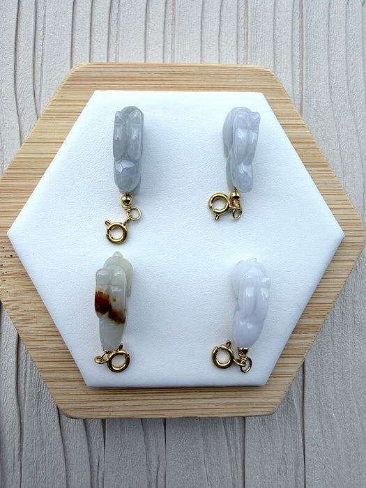 Dreamy Jade hand-carved rabbit charms in genuine jade with gold-tone clasps on a white hexagonal display stand.