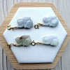 Dreamy Jade hand-carved jade rabbit charms with gold-tone clasps displayed on a white hexagonal stand.