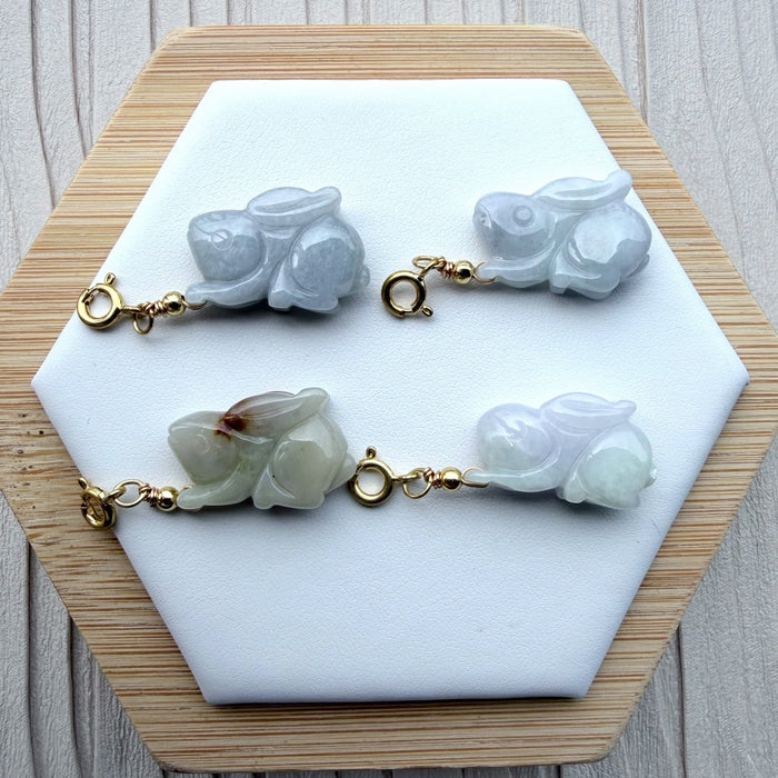 Dreamy Jade hand-carved jade rabbit charms with gold-tone clasps displayed on a white hexagonal stand.