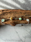 Dreamy Jade sterling silver bracelet featuring multi-coloured jade clover stones and coin charms on a wooden surface.