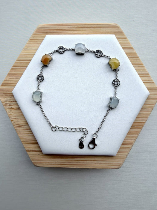 Dreamy Jade multi-coloured jade gemstone link bracelet with 925 sterling silver coin charms on a white display stand.