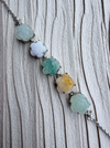 Dreamy Jade multi-coloured floral carved jade gemstone bracelet with silver-tone chain on a textured cream background.