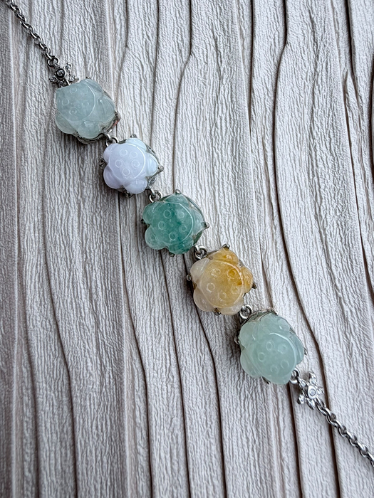Dreamy Jade multi-coloured floral carved jade gemstone bracelet with silver-tone chain on a textured cream background.