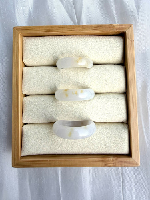 Dreamy Jade natural stone band rings with milky white and golden-yellow inclusions displayed in a wooden jewellery box.