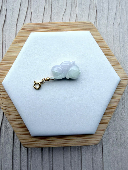 Dreamy Jade hand-carved rabbit charm in pale green jade with a gold-tone clasp on a white hexagonal display stand.
