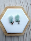 Dreamy Jade rabbit pendants in translucent green jade with rose gold and silver pavé-set stone bails on a display base.