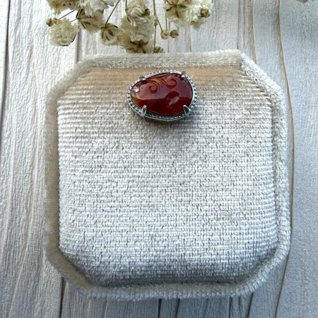 Dreamy Jade red jadeite pendant with intricate hand-carved swirling motifs set in a silver-tone frame with crystal.