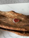 Dreamy Jade red jadeite pendant with hand-carved swirling motifs in a silver-tone frame on rustic wood