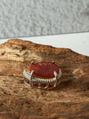 Dreamy Jade red jadeite pendant with hand-carved swirling motifs in a silver-tone frame on a textured wood surface