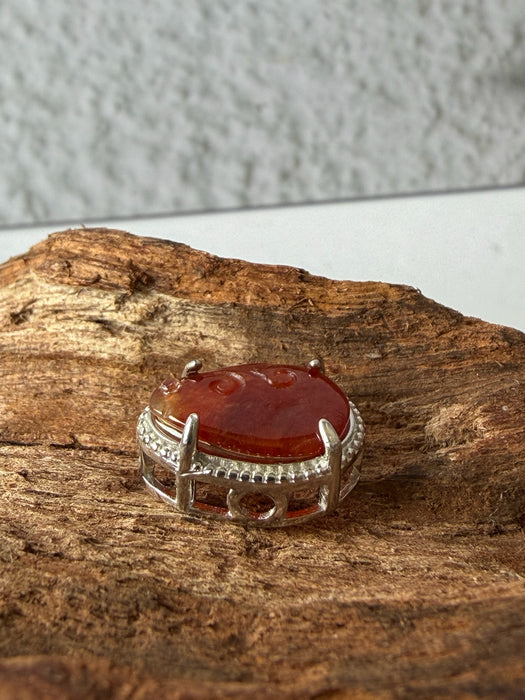 Dreamy Jade red jadeite pendant with hand-carved swirling motifs in a silver-tone frame on a textured wood surface