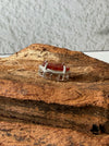 Dreamy Jade red jadeite pendant with intricate carvings in a silver-tone frame resting on textured natural wood
