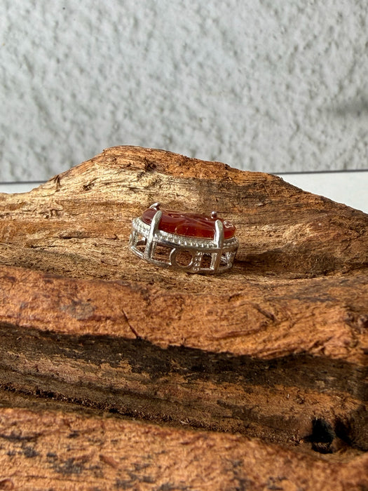 Dreamy Jade red jadeite pendant with intricate carvings in a silver-tone frame resting on textured natural wood