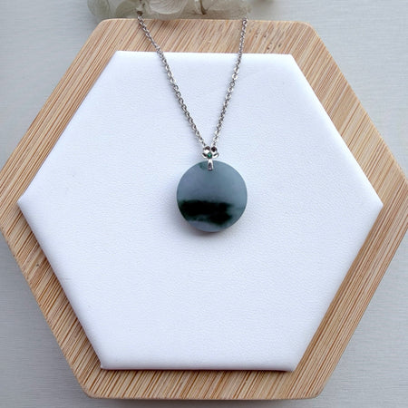 Dreamy Jade round green jade disc pendant necklace on a silver chain with a floral-inspired bail on a wooden stand.