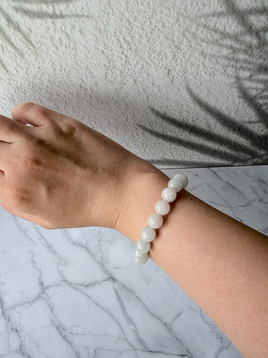 Dreamy Jade white natural jade bead bracelet worn on a wrist against a marble surface with leaf shadow