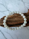 Dreamy Jade bracelet featuring polished white natural jade beads on a rustic wooden display against marble background.