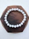 Dreamy Jade bracelet featuring smooth, polished white natural jade beads on a dark wooden hexagonal display base.