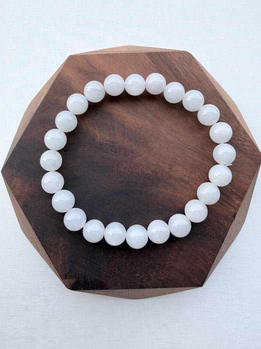 Dreamy Jade bracelet featuring smooth, polished white natural jade beads on a dark wooden hexagonal display base.